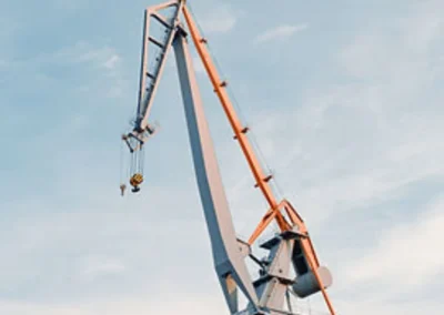 A tall, orange and grey industrial crane against a clear blue sky with some scattered clouds.